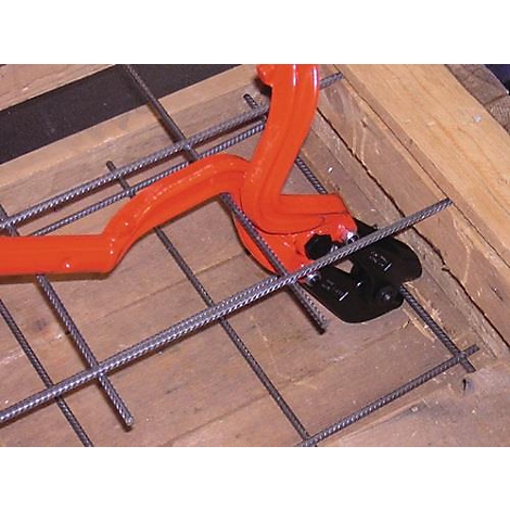 Een oranje wapeningsijzersnijder snijdt door stalen staven die op een houten frame liggen.