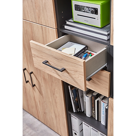 Nahaufnahme einer geöffneten Holzschublade, gefüllt mit Bürobedarf, über einem Regal mit Büchern und einem grünen Radio.