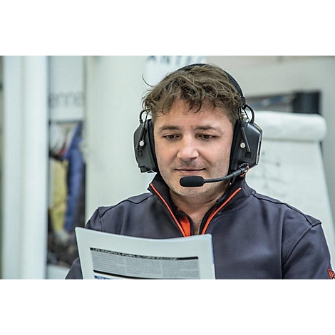 Een man met een koptelefoon leest een document, naar beneden kijkend. Hij draagt een donkerblauwe trui met een oranje accent.