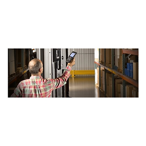 Ein Mann mit kariertem Hemd scannt mit einem Handscanner im Lager Waren. Rechts sind Regale mit Kartons zu sehen.