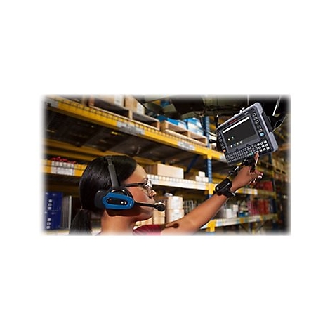 Eine Frau mit Headset bedient ein Gerät in einem Lager. Regale im Hintergrund. Die Frau zeigt auf den Bildschirm.