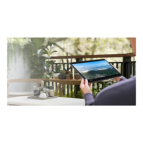 Person hält Tablet, das ein Video mit Landschaftsaufnahmen zeigt. Auf einem Tisch ist ein Kaffee-Set platziert.