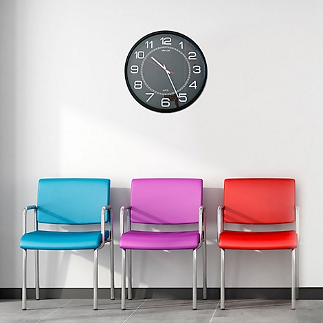 Trois chaises colorées devant un mur blanc, au-dessus d'une horloge.