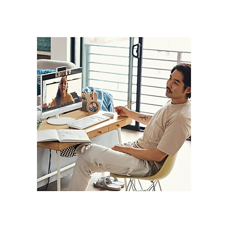 Ein Mann sitzt an einem Schreibtisch und nimmt an einer Videokonferenz teil. Auf dem Monitor ist eine Frau zu sehen. Auf dem Tisch liegen Stifte und ein Notizbuch.