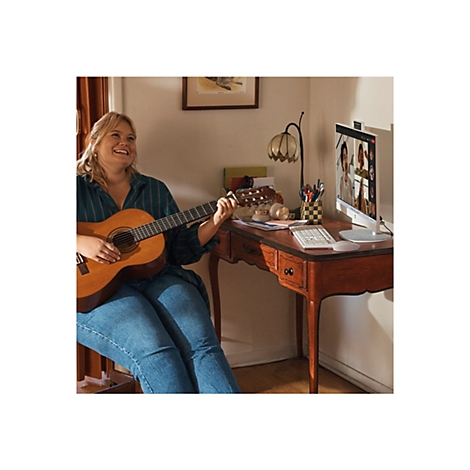 Eine lächelnde Frau spielt Gitarre und nimmt an einem Videoanruf an ihrem Schreibtisch teil.