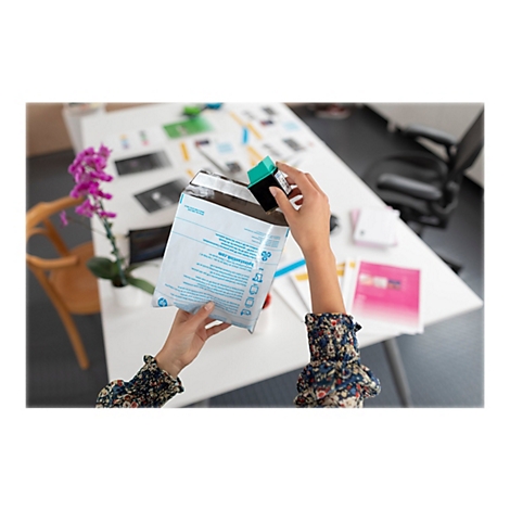 Mains tenant une enveloppe et une cartouche d'encre. Des documents et une orchidÃ©e sont sur la table.
