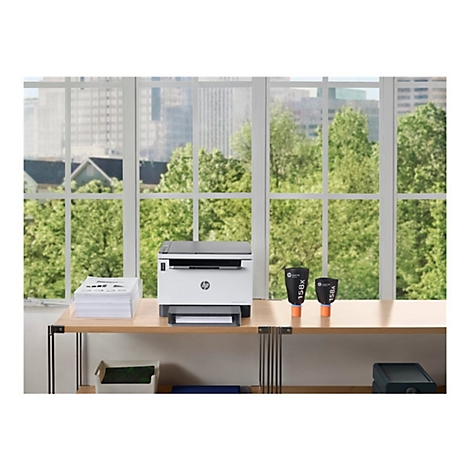 Büro mit HP Drucker, Papierstapel und Tintenpatronen vor Fenster mit Blick auf Bäume und Gebäude.