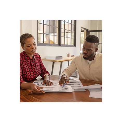 Deux personnes regardent des documents ensemble Ã  une table. Une femme en chemise rouge, un homme en pull beige.