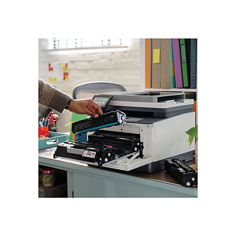 Eine Person tauscht eine blaue Tonerkartusche in einem Multifunktionsdrucker aus. Der Drucker steht auf einem Schreibtisch.