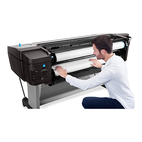 Ein Mann kniet vor einem großformatigen Drucker und legt Papier ein.