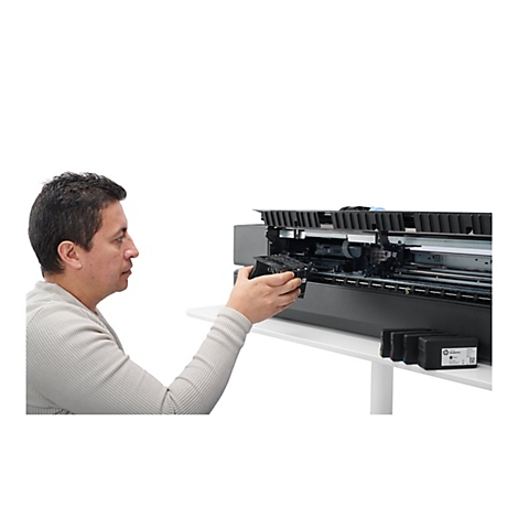 Ein Mann tauscht eine schwarze Tintenpatrone in einem grossen Tintenstrahldrucker aus. Der Drucker und die Tintenpatrone sind auf einem weissen Tisch vor weissem Hintergrund.