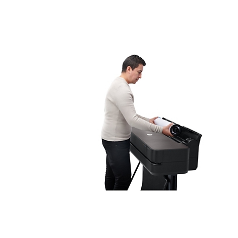 Un homme insère un rouleau de papier dans une imprimante grand format. Il porte un pull clair et un jean noir. Le fond est blanc.
