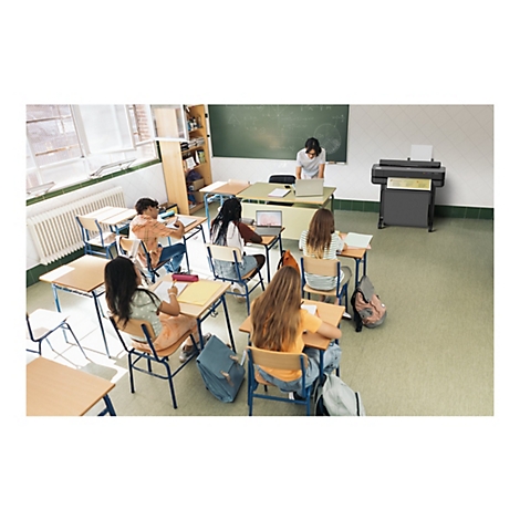 Ein Klassenzimmer, in dem Schüler an ihren Tischen arbeiten. Eine Lehrerin steht am Whiteboard. Rechts steht ein großer Drucker.