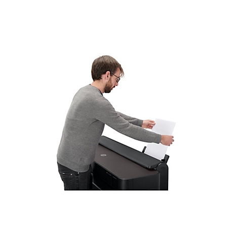 Ein Mann mit Brille legt Papier in einen schwarzen Drucker. Er trägt ein graues Sweatshirt und Jeans.
