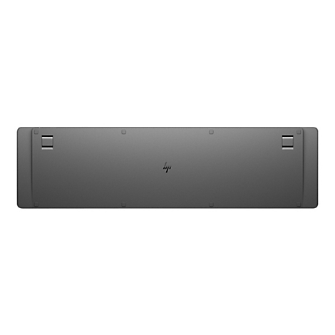 Die Unterseite einer grauen HP-Tastatur mit zwei ausklappbaren Standfüßen und dem mittigen HP-Logo.