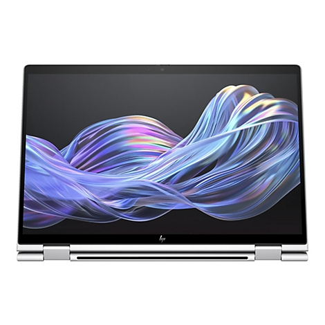 Ein Laptop mit silbernem Gehäuse, geöffnet. Auf dem Bildschirm sind fließende, farbige Wellen vor dunklem Hintergrund zu sehen.