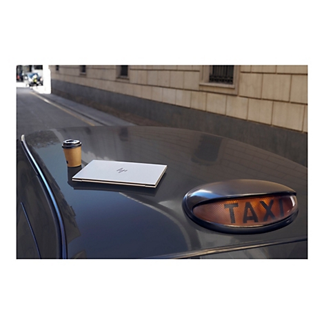 Ein Laptop und ein Pappbecher stehen auf einem Taxi. Im Hintergrund ein Straßenzug.