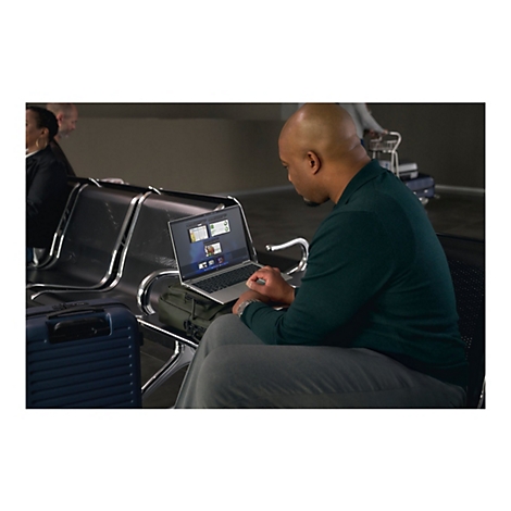 Ein Mann sitzt in einem Wartebereich und arbeitet mit seinem Laptop. Neben ihm ist Gepäck platziert.