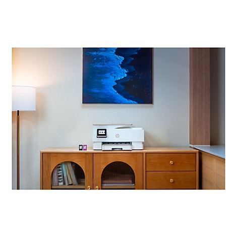 Ein weißer HP Drucker steht auf einer Holzkommode. Darüber hängt ein blaues abstraktes Bild. Links eine goldene Stehlampe.
