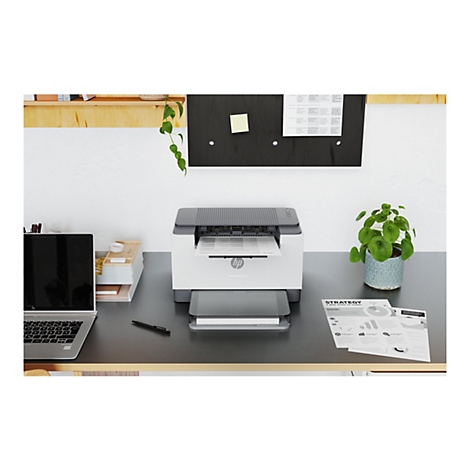Weißer HP-Laserdrucker mit einem Blatt Papier, schwarzem Laptop und Bürozubehör auf einem Schreibtisch, Hintergrund weiß und Holz.