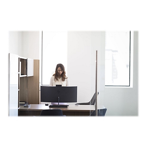 Eine Frau mit Brille sitzt an einem Schreibtisch und arbeitet an einem groÃŸen Computerbildschirm in einem modernen BÃ¼ro.