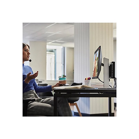 Eine Frau mit Headset sitzt vor einem Monitor, wÃ¤hrend sie einen Becher hÃ¤lt. Auf dem Monitor ist ein Videoanruf zu sehen.