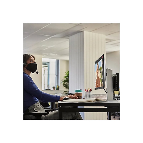 Eine Frau mit Maske und Headset sitzt am Computer, sie nimmt an einer Videokonferenz teil.