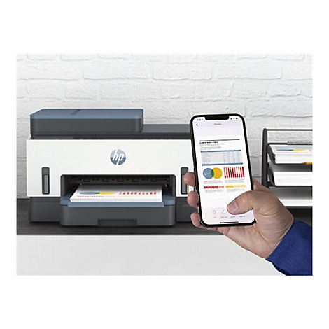 Une personne tient un smartphone affichant un document devant une imprimante HP. L'imprimante et le téléphone sont sur un bureau contre un mur de briques.