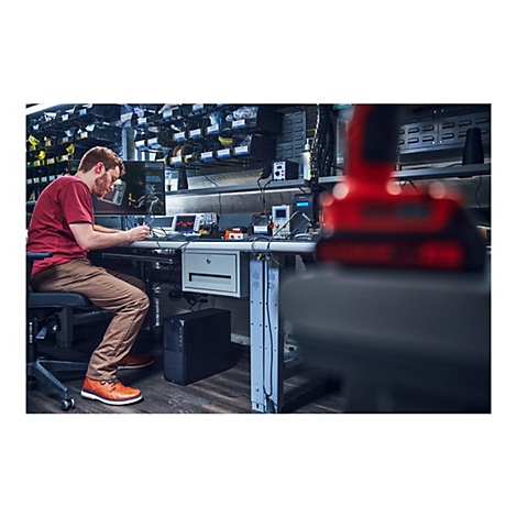 Ein Mann arbeitet an einem Schreibtisch mit elektronischen GerÃ¤ten, wÃ¤hrend im Vordergrund ein rotes Werkzeug unscharf ist.