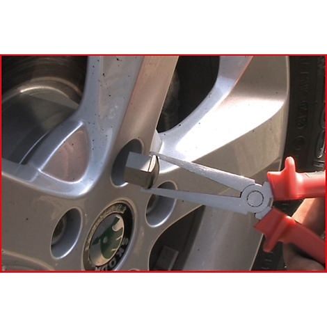 Nahaufnahme: Zange an einem silbernen Autoreifen, der ein Radmutter herausnimmt.