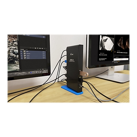 Hub USB noir avec cÃ¢bles connectÃ©s et une clÃ© USB. Deux moniteurs sont posÃ©s sur un bureau en bois.