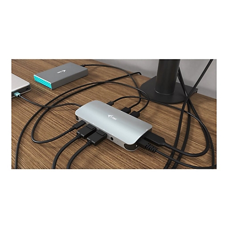Hub USB-C argentÃ© avec cÃ¢bles connectÃ©s et un ordinateur portable sur une surface en bois. Un moniteur en arriÃ¨re-plan.