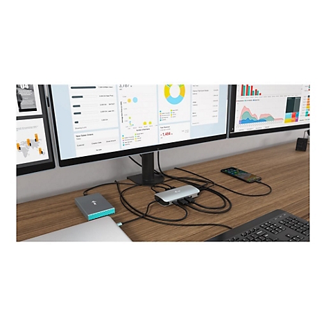 Plusieurs moniteurs sur un bureau en bois, connectÃ©s Ã  un hub et Ã  des accessoires. Des graphiques sont visibles sur les moniteurs.