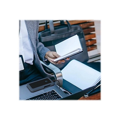 Person mit Laptop, Notizbuch und externer Festplatte. Sie sitzt draußen auf einer Bank mit Tasche im Hintergrund.
