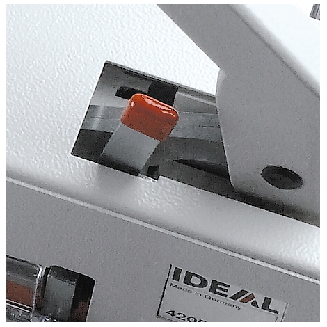 Close-up of a white machine with an orange button. In the lower part, a sign with the inscription 'IDEAL, Made in Germany' is visible.