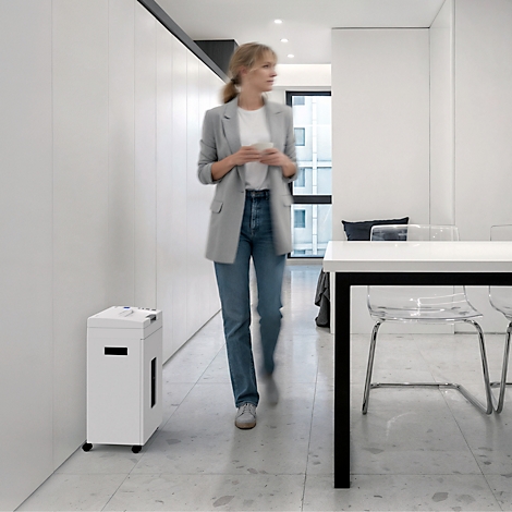 Een vrouw loopt langs een papierversnipperaar in een modern kantoor.