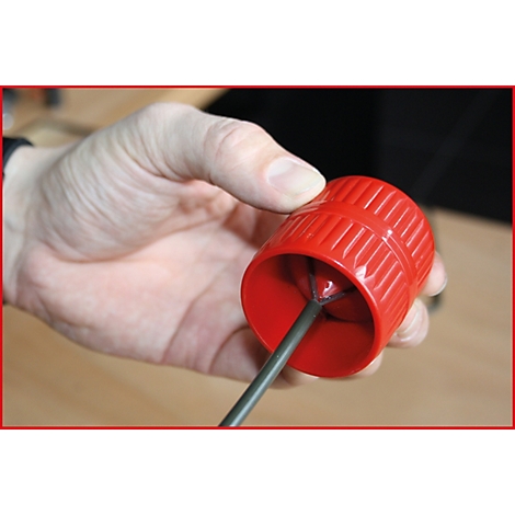 Eine Hand hält ein rotes Werkzeug, in dem ein grauer Stab steckt. Das Werkzeug hat geriffelte Oberflächen. Der Hintergrund ist unscharf.