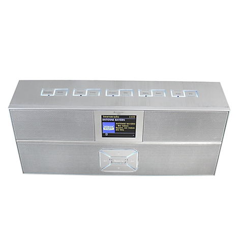 Silver digital radio with screen, top controls and a logo. The display shows a radio station.