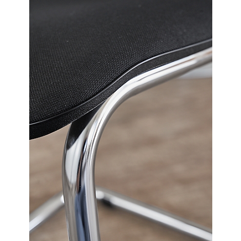 Close-up of a chair, with a black fabric seat, and a chrome metal frame.