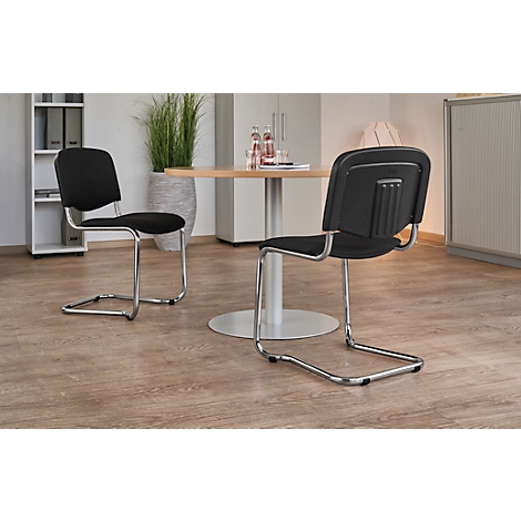 Two black chairs with chrome frames in a room with light wooden floors. A table in the background.