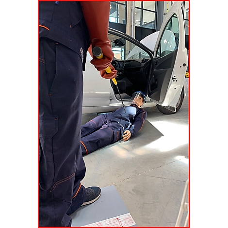 Eine Person in blauer Kleidung hält einen Hammer und steht über einer Person, die auf dem Boden liegt. Hinter ihnen ein geöffnetes Autofenster.