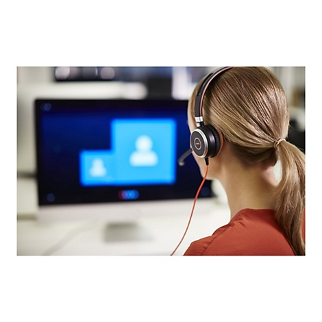 Eine Person mit Headset, die vor einem Bildschirm sitzt, an einem Videoanruf teilnimmt.