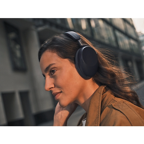 Une femme portant un casque noir marche à l'extérieur. Elle sourit, avec des bâtiments en arrière-plan.