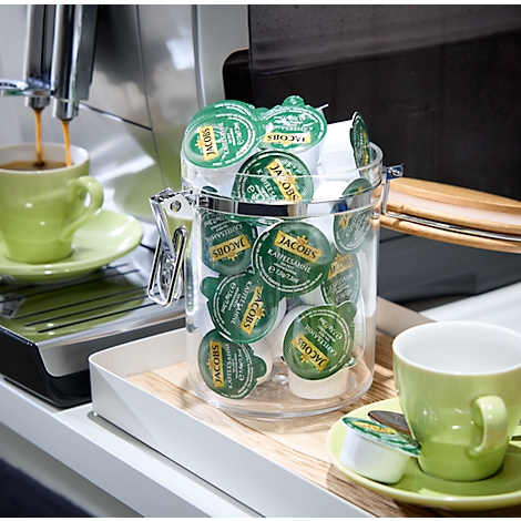 A coffee machine brewing coffee into a green cup, next to a jar of Jacobs coffee capsules.