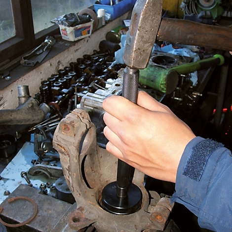 Une main utilise un marteau et un chasse-goupille pour insérer un roulement dans une pièce automobile.