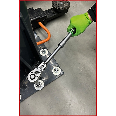Une main portant un gant vert vif utilise un cliquet pour serrer un boulon sur une base de machine.