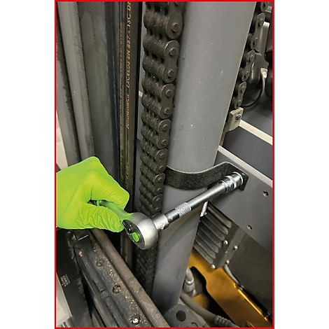 Main avec un gant jaune fluo utilisant un cliquet sur un assemblage technique à chaîne.