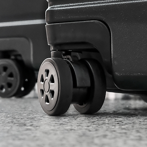Gros plan sur les roues d'une valise noire sur une surface grise. L'accent est mis sur les roues.