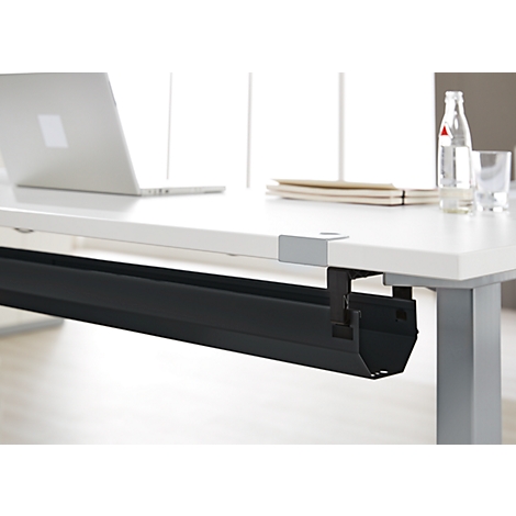 Bureau met kabelgoot. Een zwarte kabelgoot is bevestigd onder een wit tafelblad. Op de tafel liggen een laptop, waterfles, papier.
