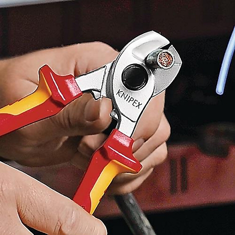 Persoon snijdt een kabel door met een krimptang. De tang heeft rode en gele handgrepen en de tekst KNIPEX.
